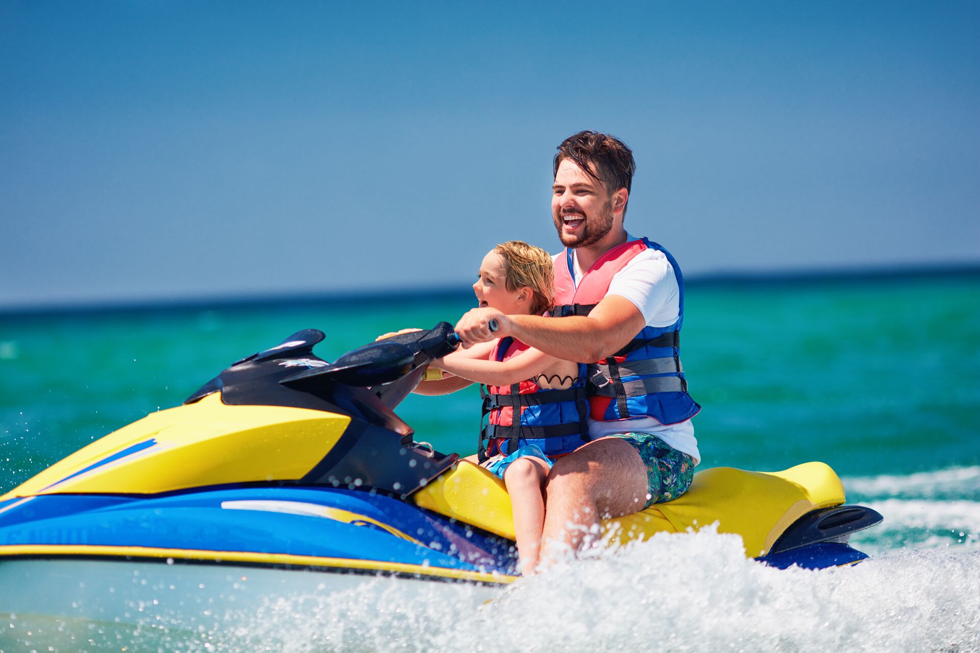 A smiling man drives a jet ski with a child. 