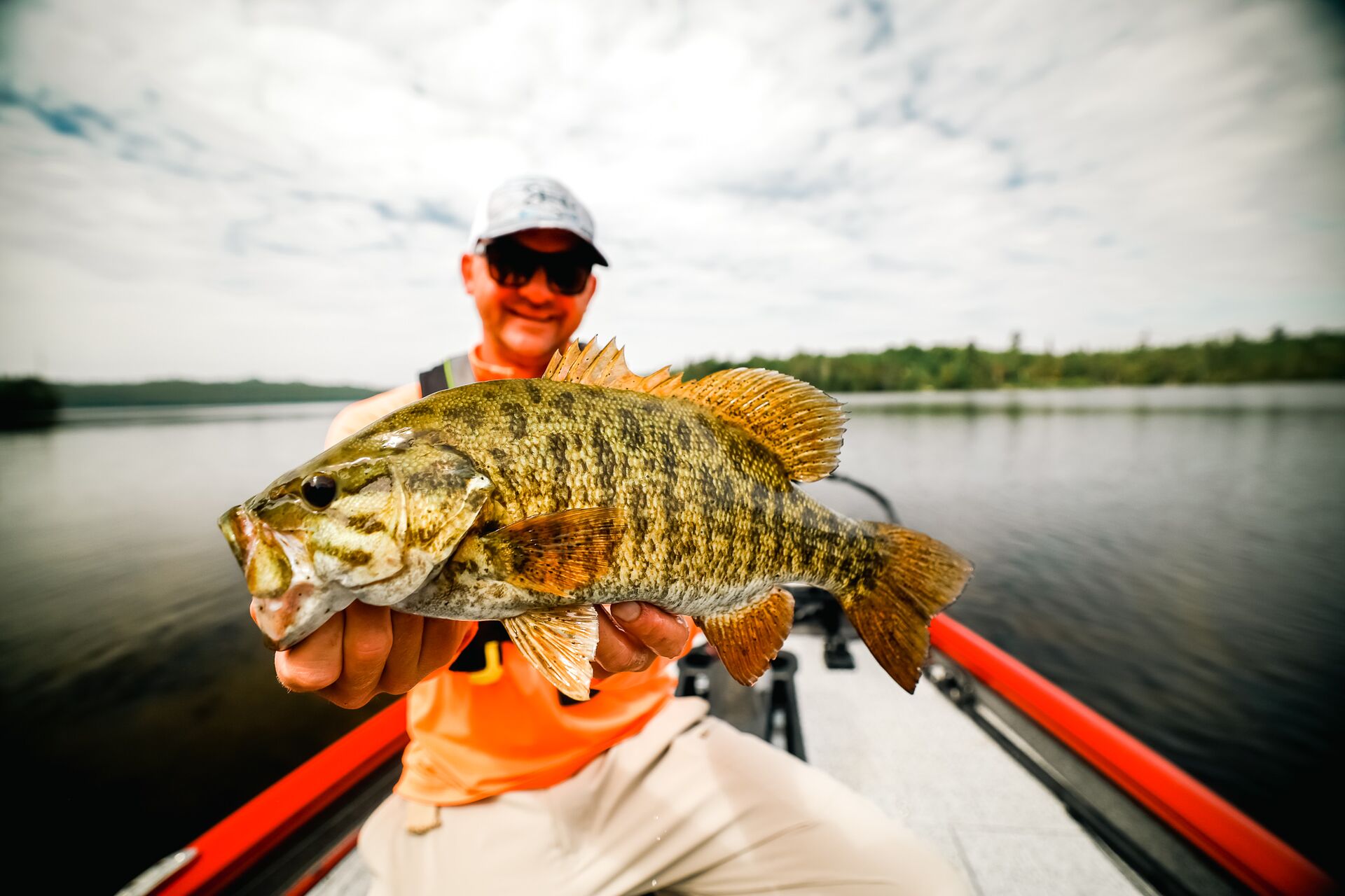 Man holds up a fish while on a boat on a lake.