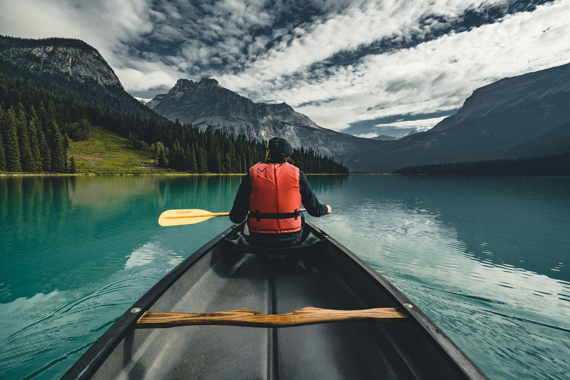 Guy in canoe with orange life vest and mountains ahead of him.