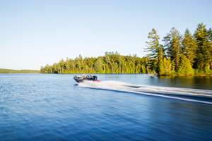 Fishing boat moves across lake with trees on shore, best boating lakes concept.