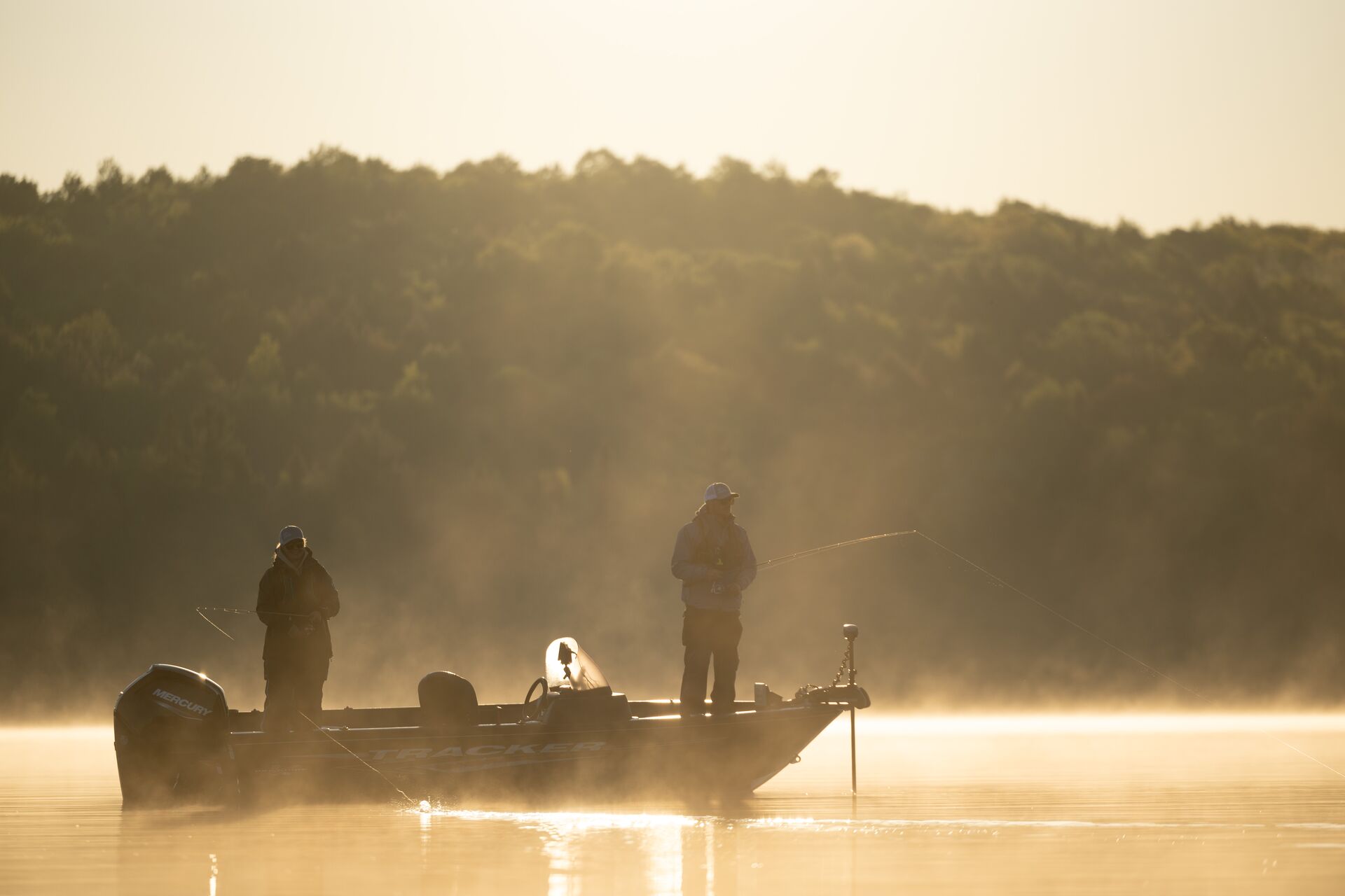 Two people fishing from a boat on a lake in the morning fog.