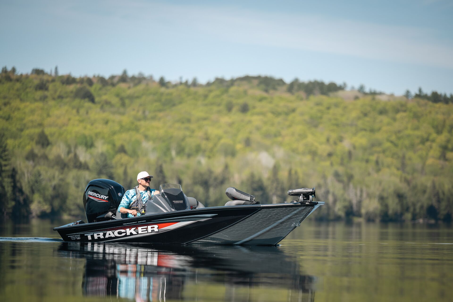 Man drives a black bass boat on a lake with trees nearby, get a Nevada boating license concept. 