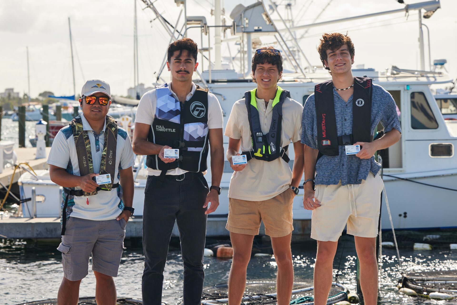 Four guys with boater safety cards wearing life jackets on dock. 