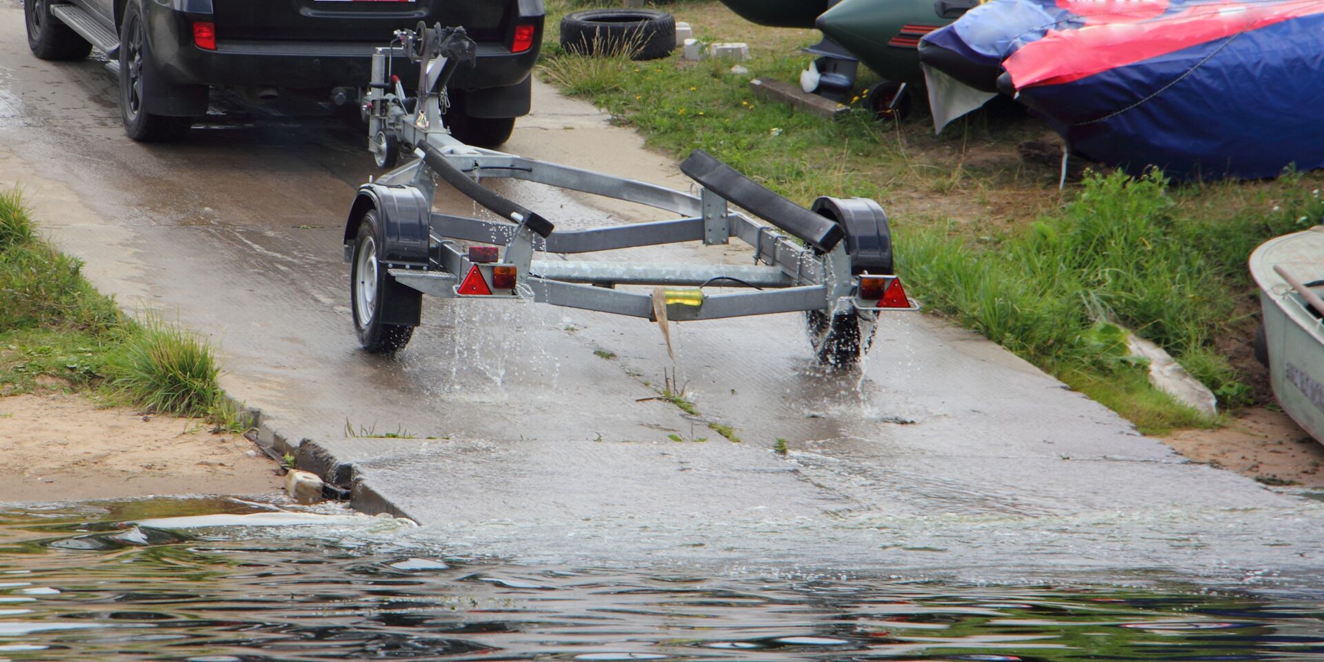An empty boat trailer attached to a truck while on a boat ramp.