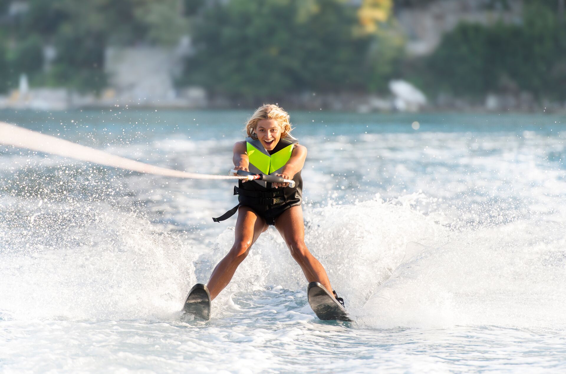 A girl wearing a life vest while on water skis behind a boat.