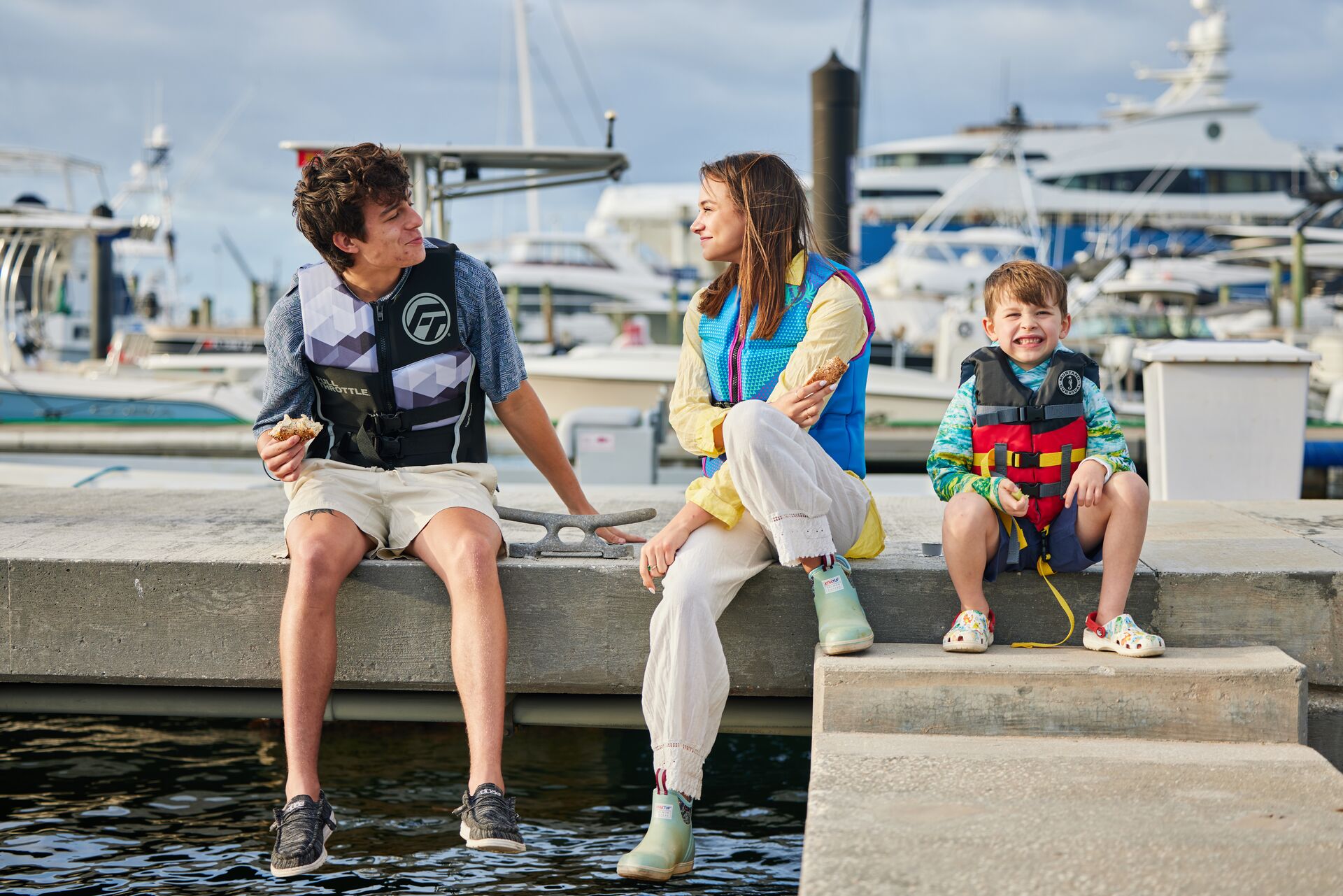 Three different sized kids in life jackets on a dock.