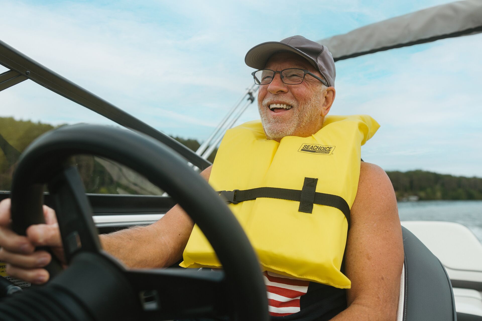 A man smiles, wearing a yellow PFD, driving a boat, proper life jacket fit concept. 