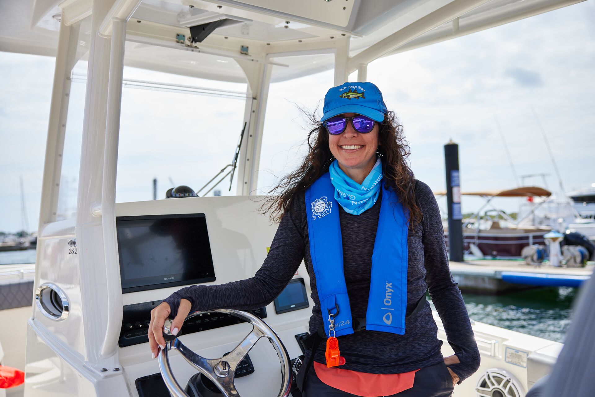 A woman smiles at the helm of a boat and wears a blue inflatable PFD.