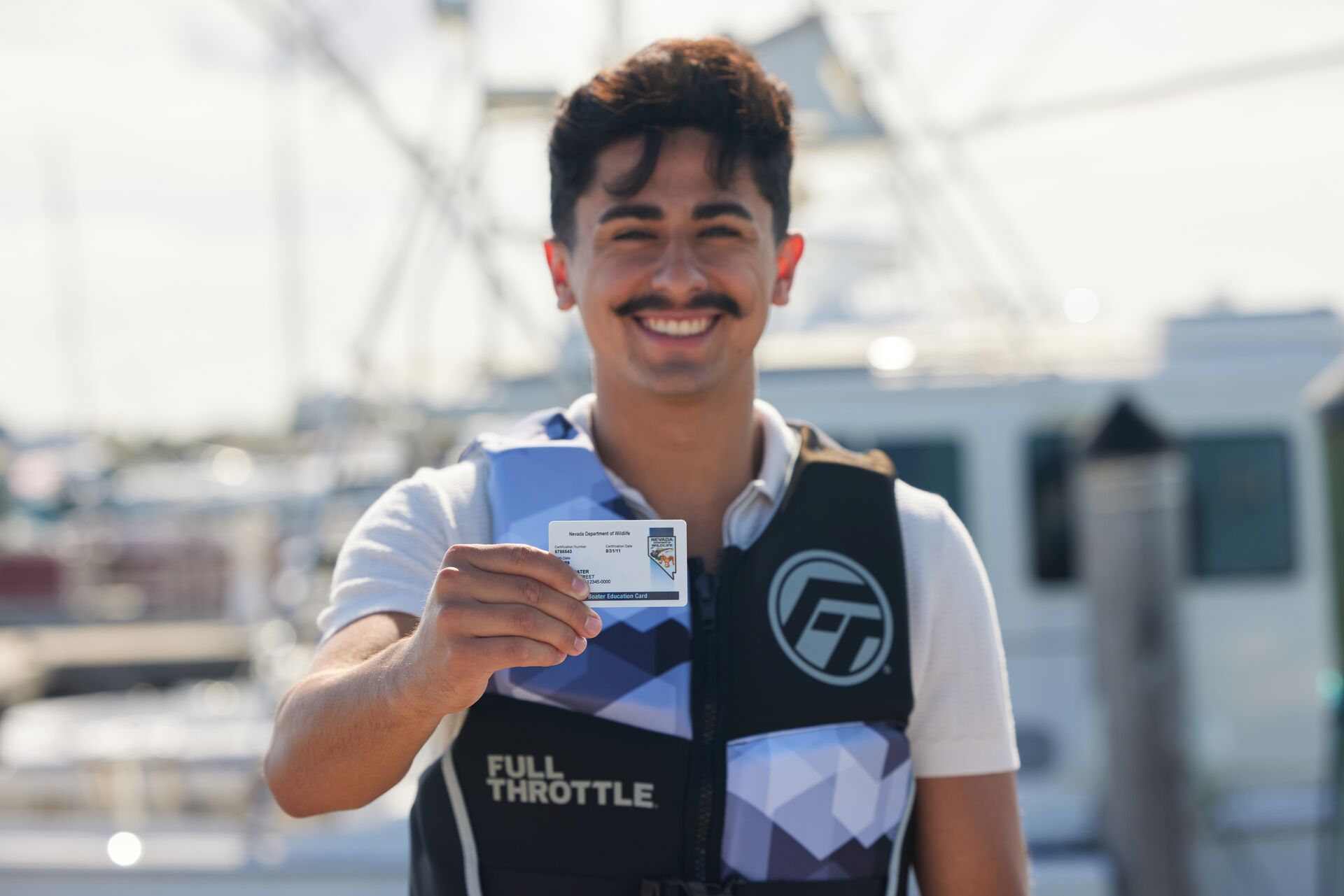 A smiling man in a life jacket holds a boater card, boater safety equipment checklist concept. 