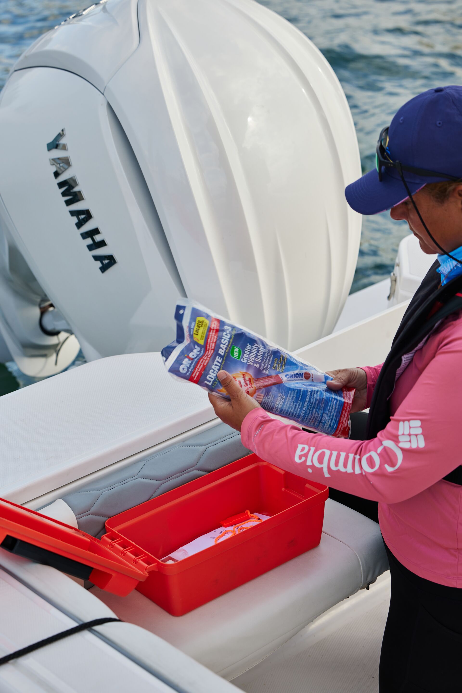 A woman wearing a life jacket checks a distress signal in a box on a boat. 