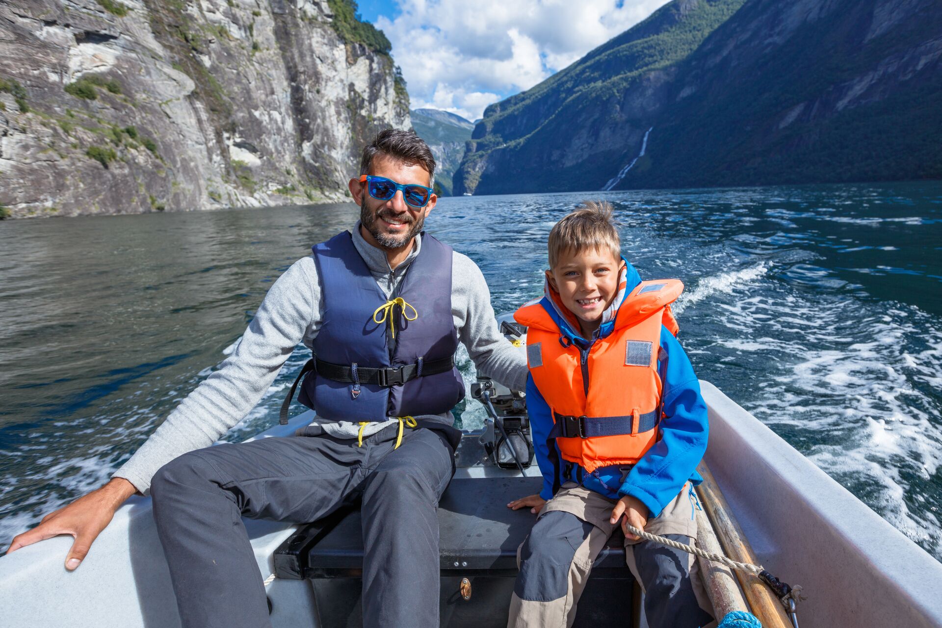 A man and boy wearing life jackets on a boat in what looks like cold temperatures.