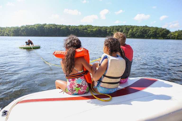 A few kids on the back of a boat holding a line pulling in a person on a tube. 
