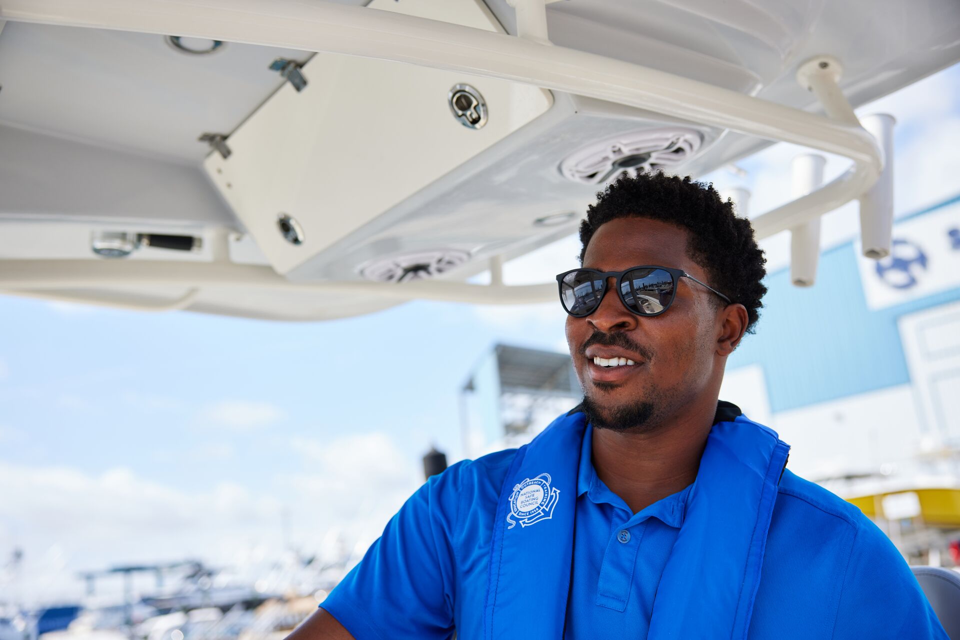 A smiling man wears a blue life jacket while driving a boat, boating safety tips for beginners concept.