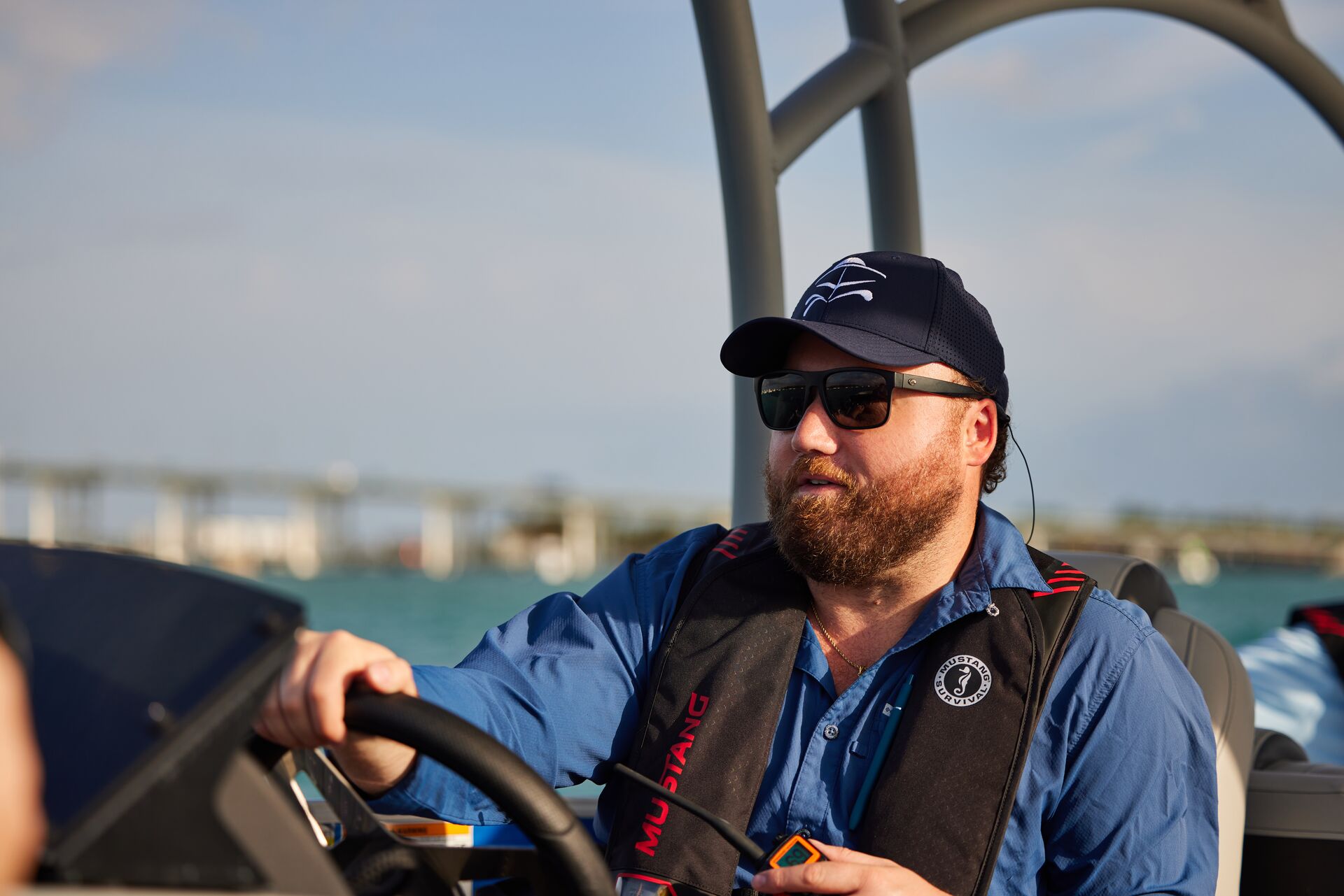 A man in a black live vest drives a boat, do boating licenses transfer between states concept.
