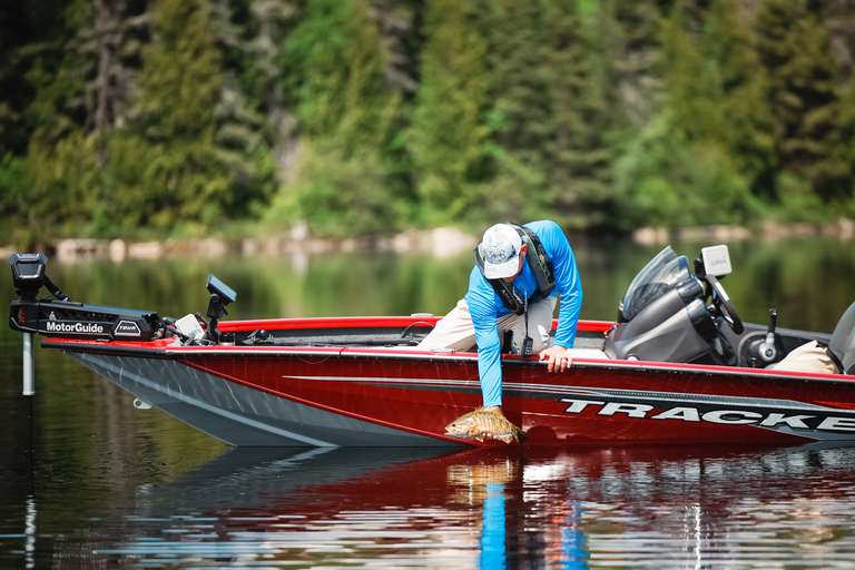 An angler pulls a fish into a red fiberglass fishing boat.