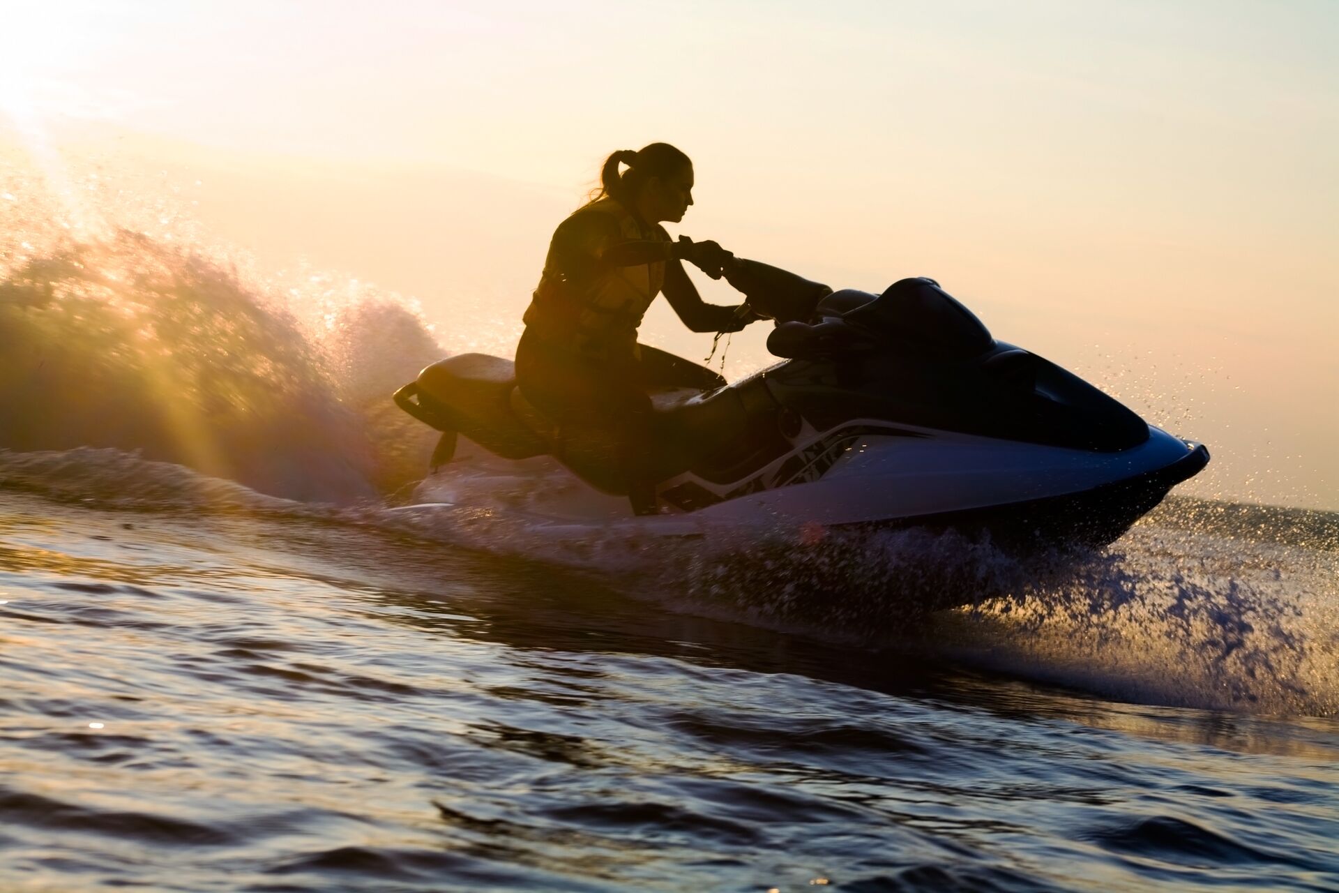 The silhouette of a girl on a jet ski with the sun behind her.