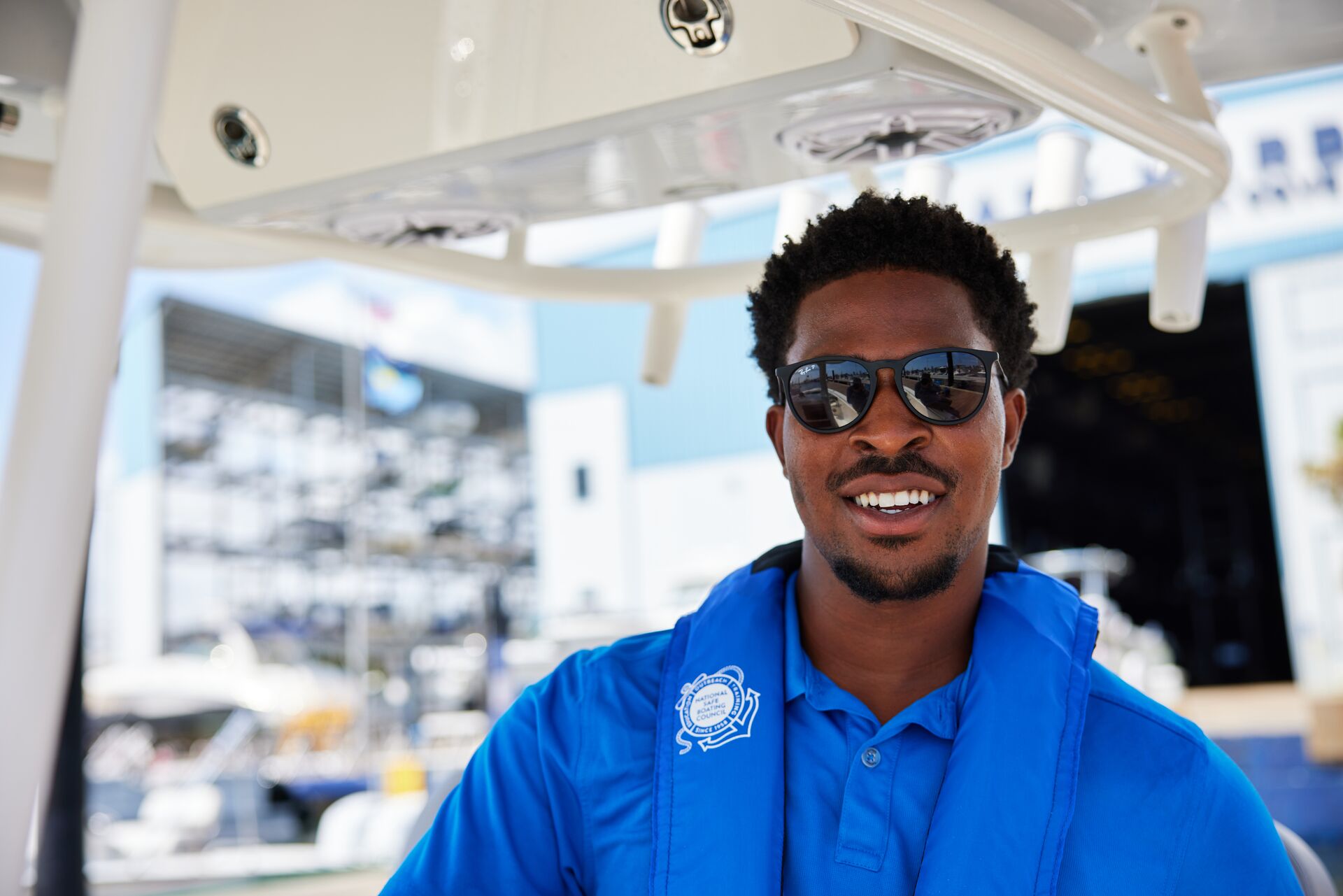 Man at the helm of a boat smiles while wearing a blue life vest.