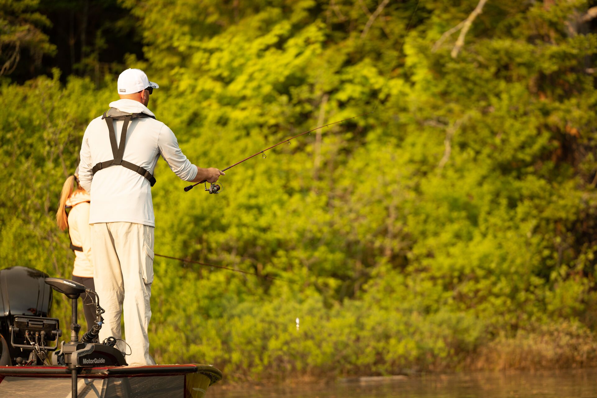 Angler on a boat near shore casting a line, fishing and boating in shallow water concept.
