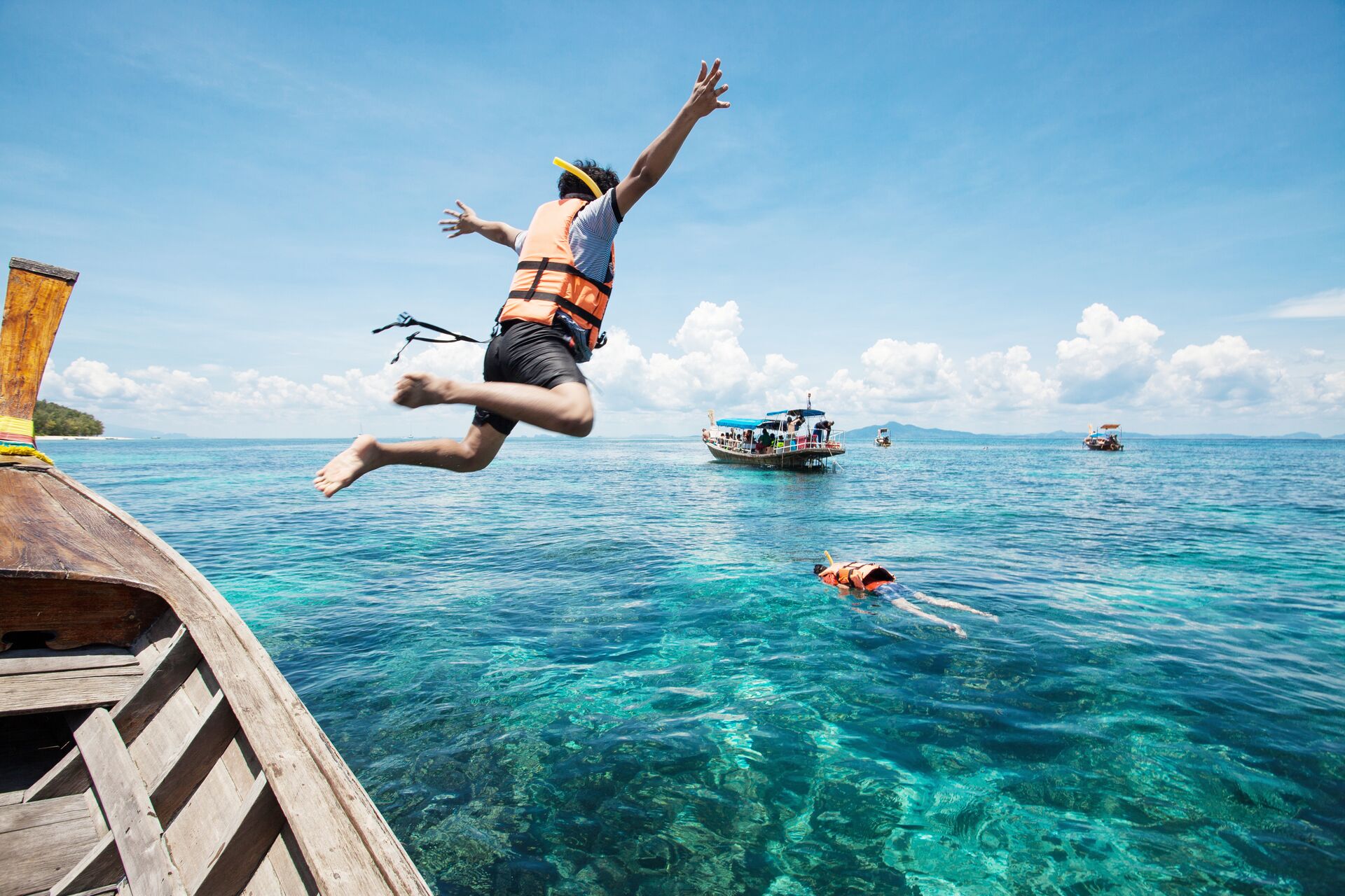 Kids jump from a boat in shallow water.