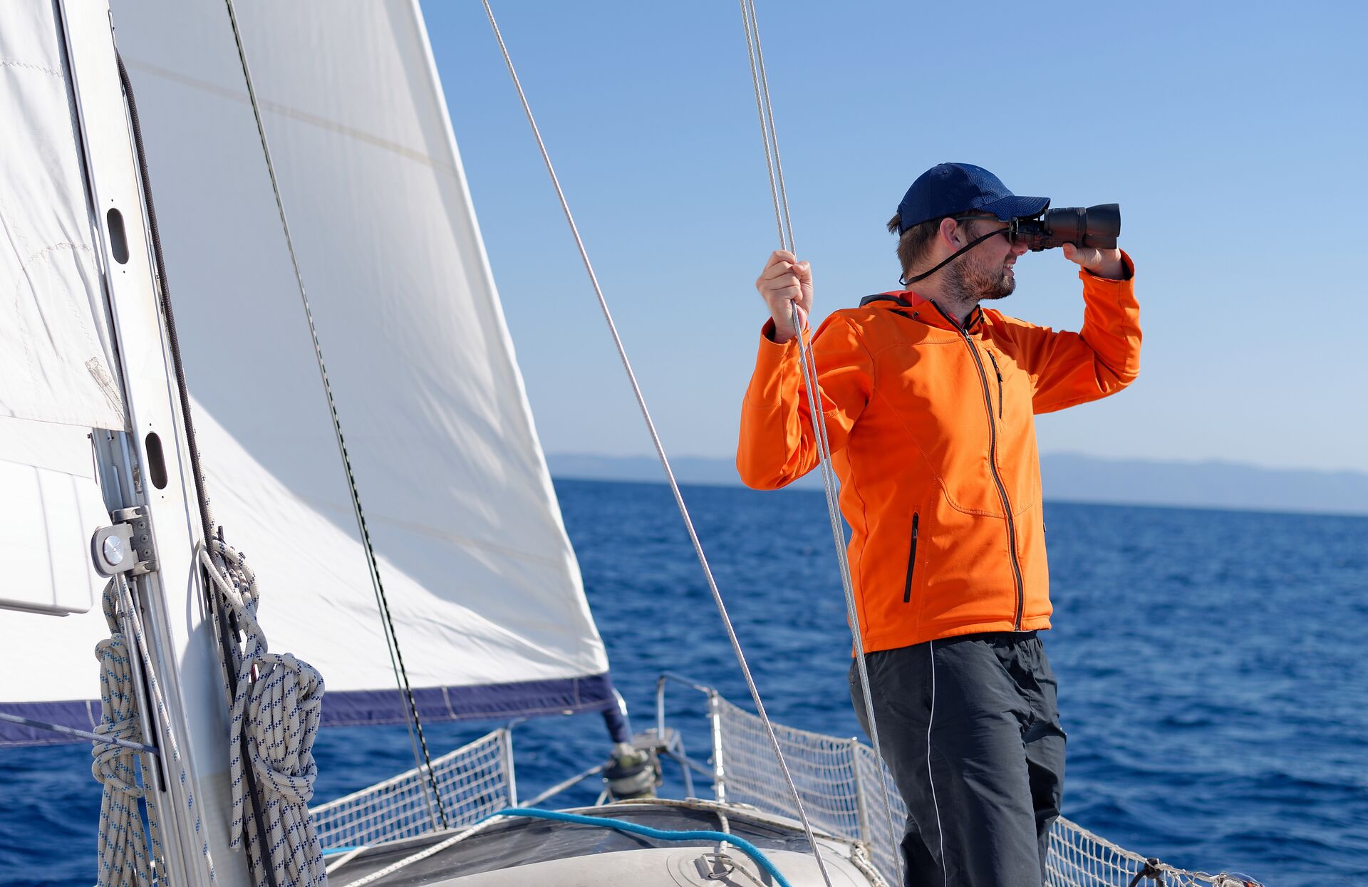 A man using binoculars on a sailboat, how to read a nautical map concept.