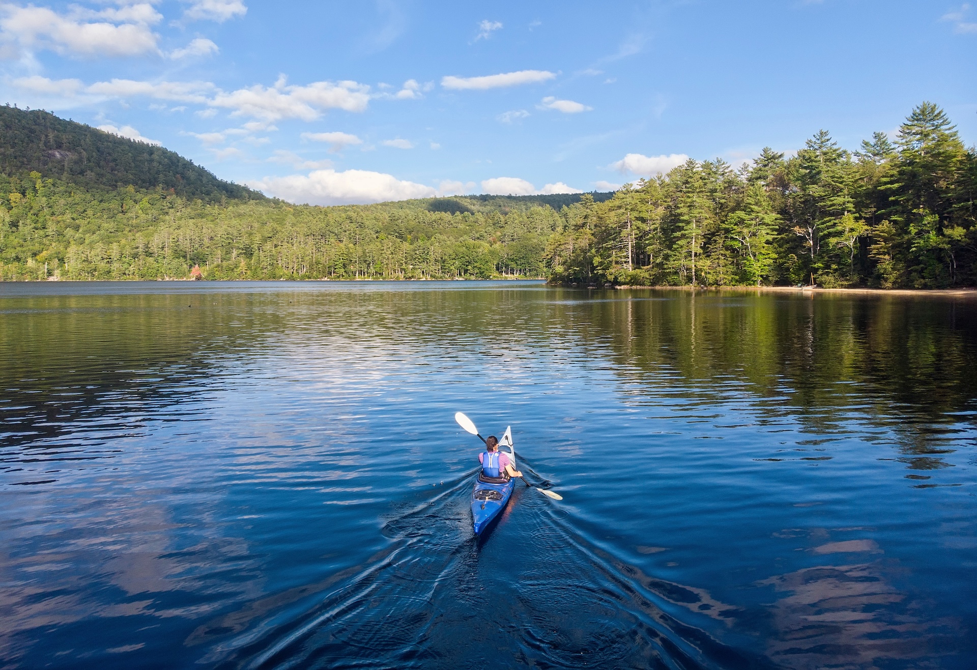 Person kayaking on river surrounded by trees, represents Umbagog National Wildlife Refuge