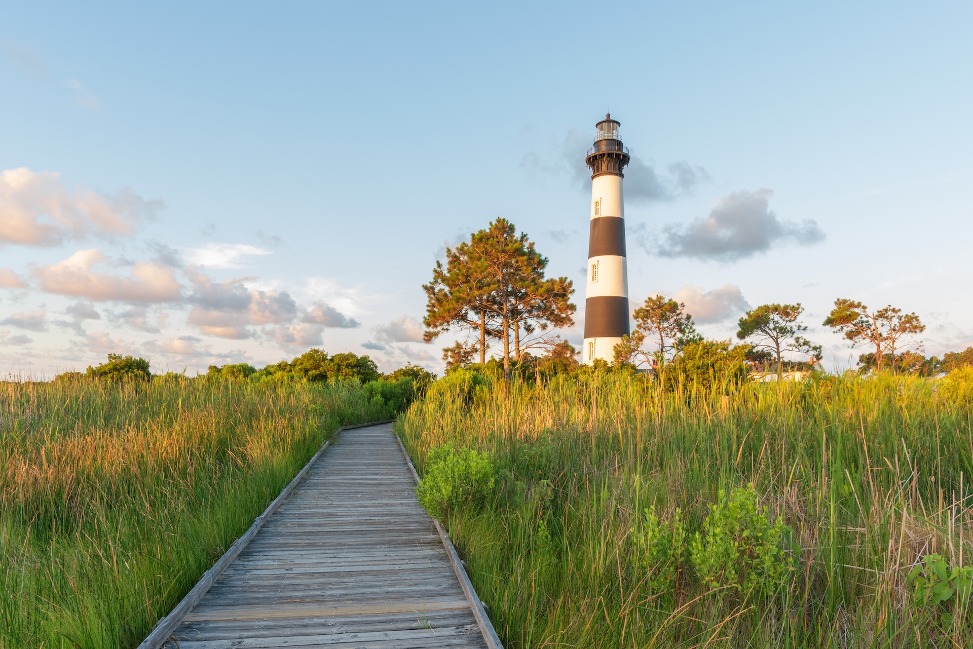 Lighthouse across field with wooden bridge nearby.