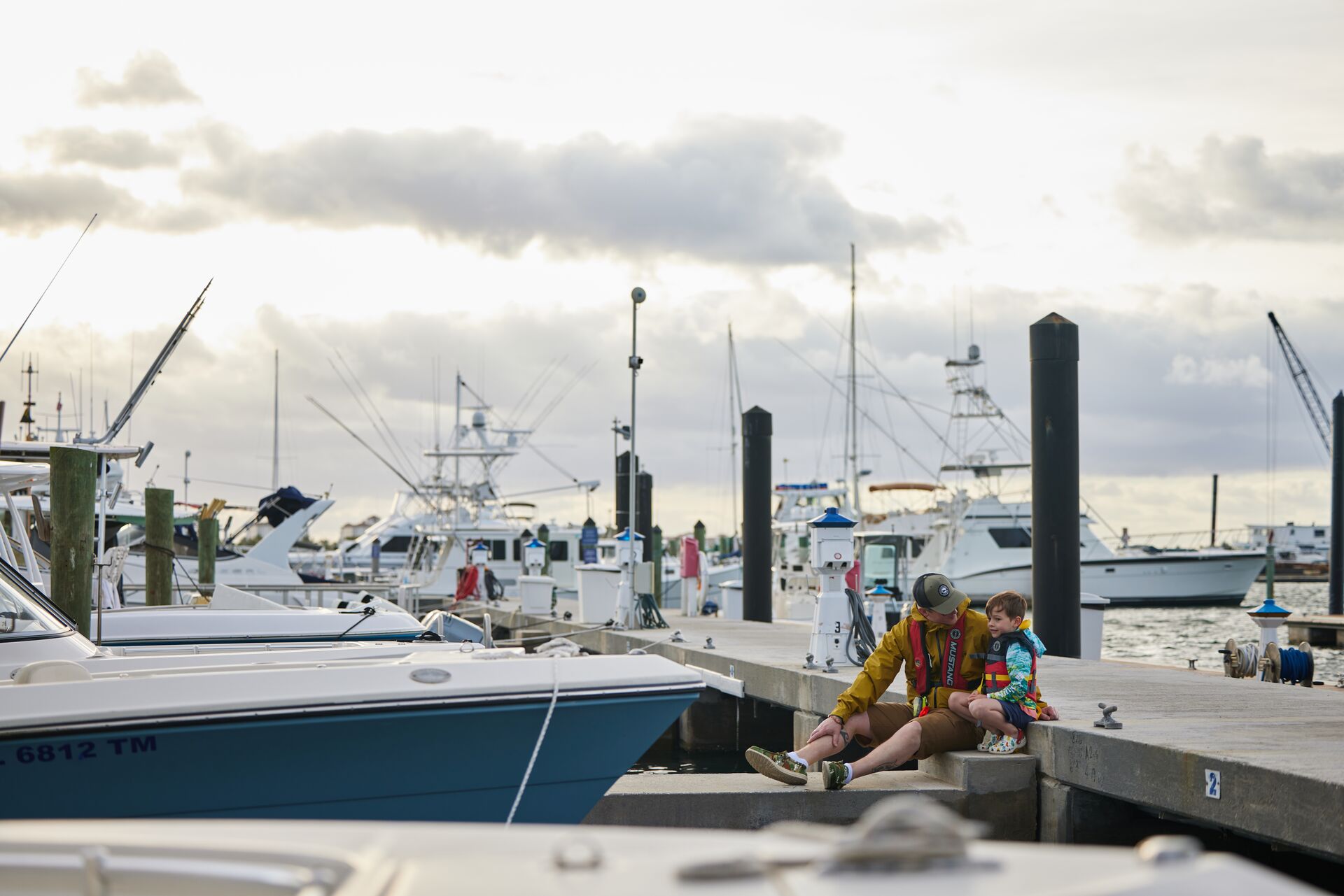 A man and boy sit on a marina near boats, Texas boat registration concept.