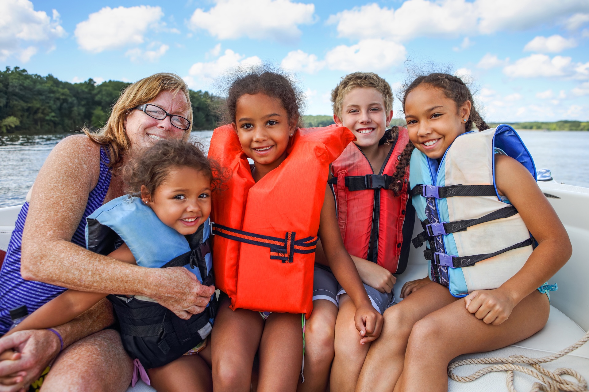 Kids and woman wearing life jackets on a boat.