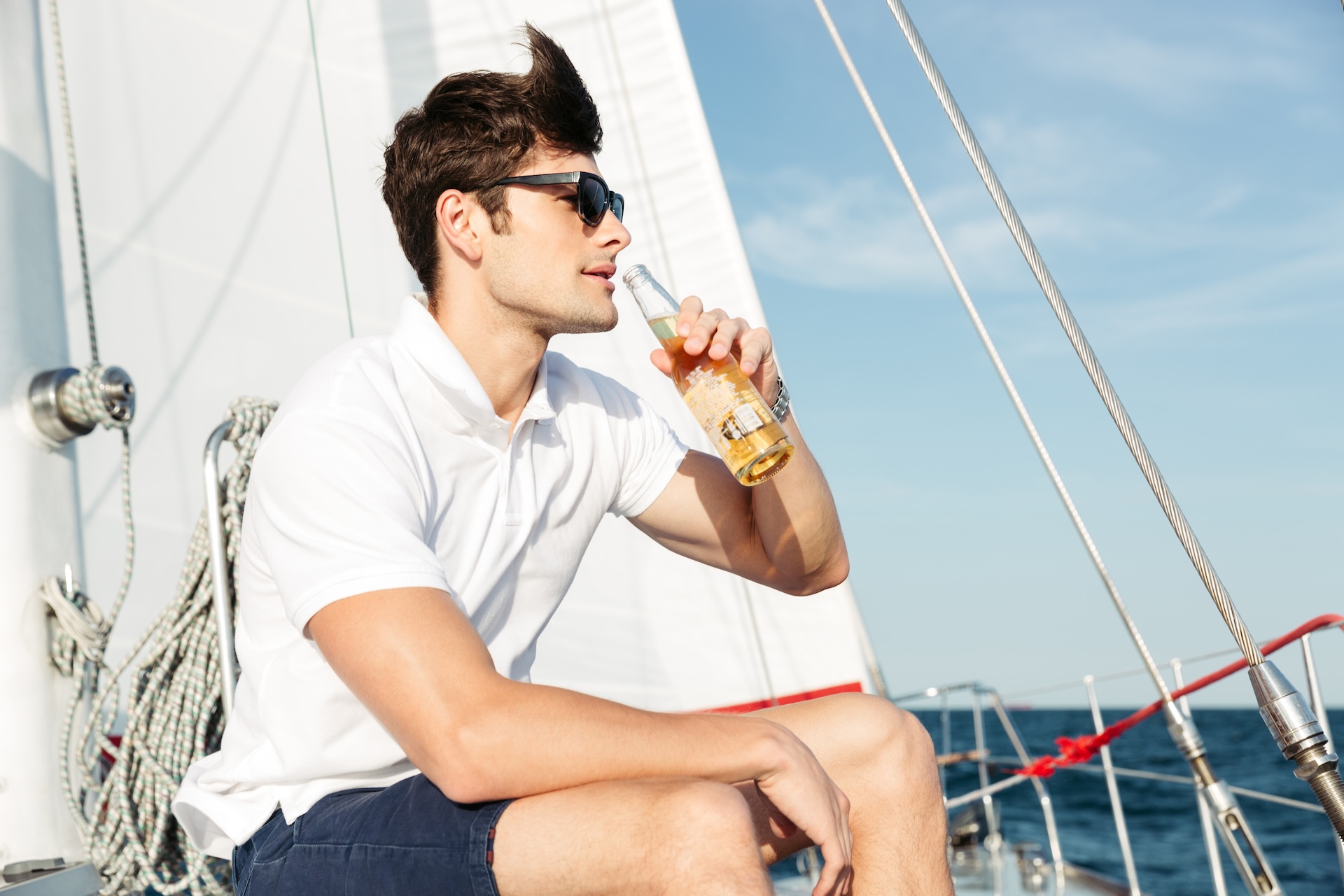 A guy drinking from a beer bottle on a boat, know boat drinking laws concept. 
