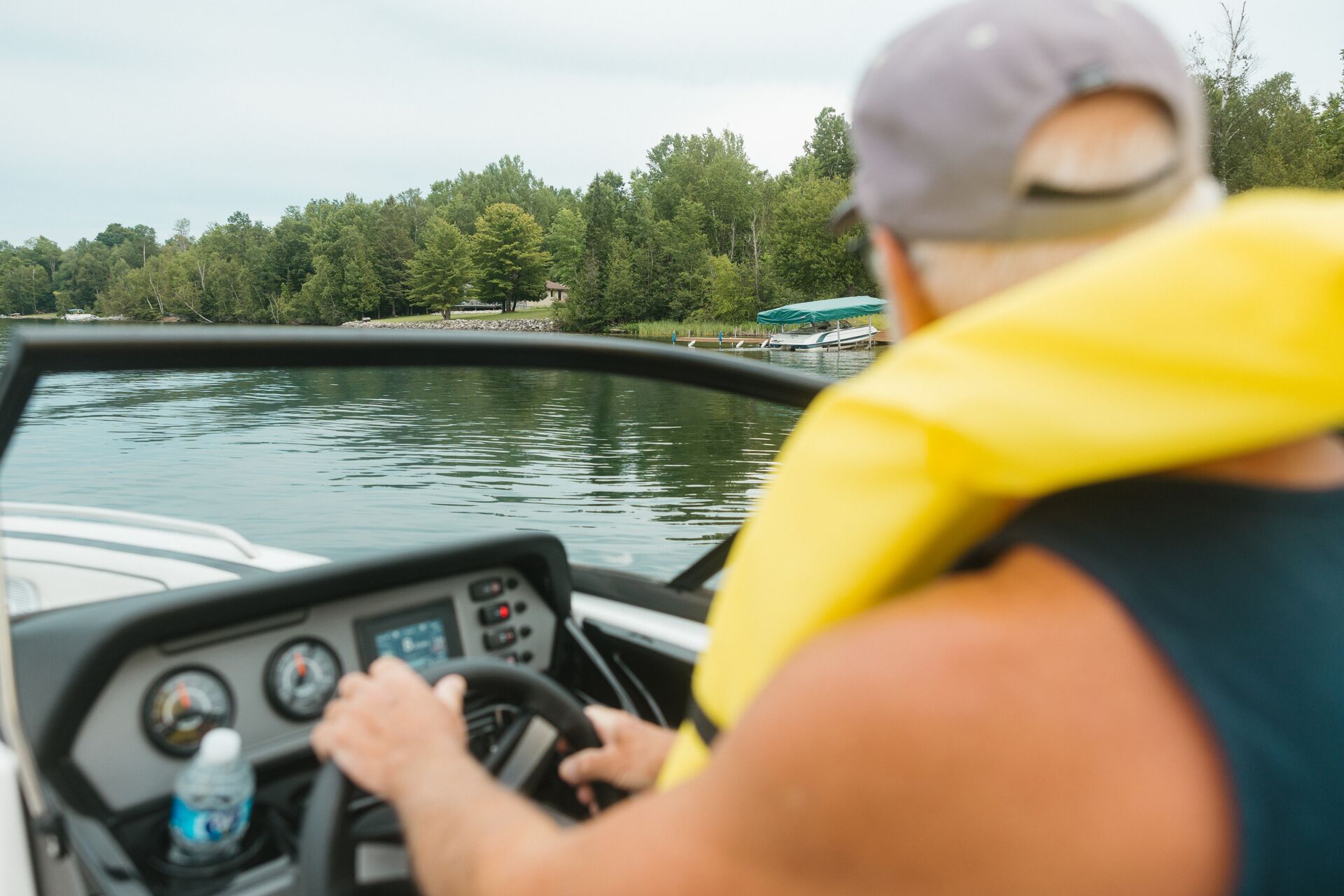 Man in yellow life vest drive boat near shore. 