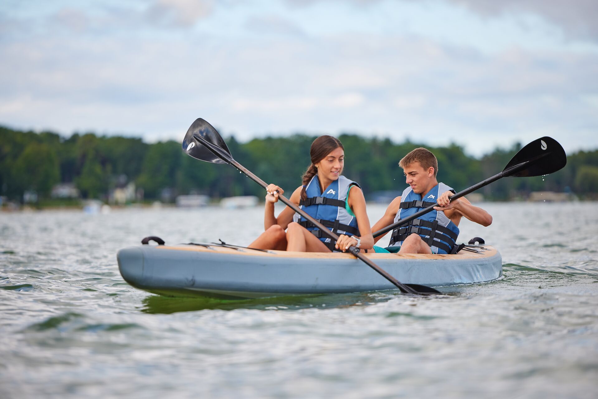 Girl and boy paddling a kayak while wearing life vests. 