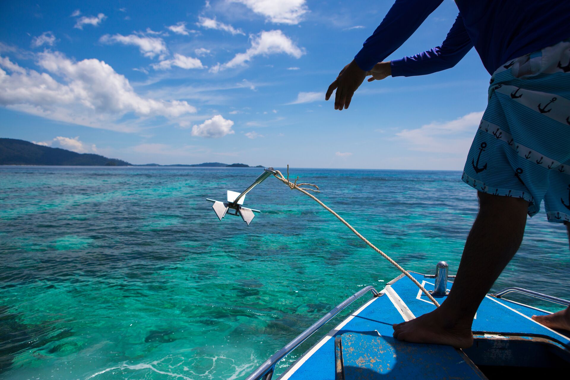 Person throwing anchor off front of boat, anchoring a boat concept.