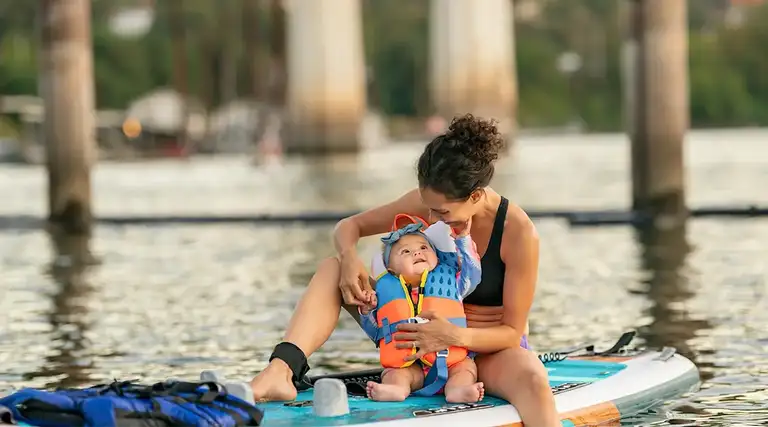 Woman on paddle board with infant in life jacket, best infant life jacket concept.