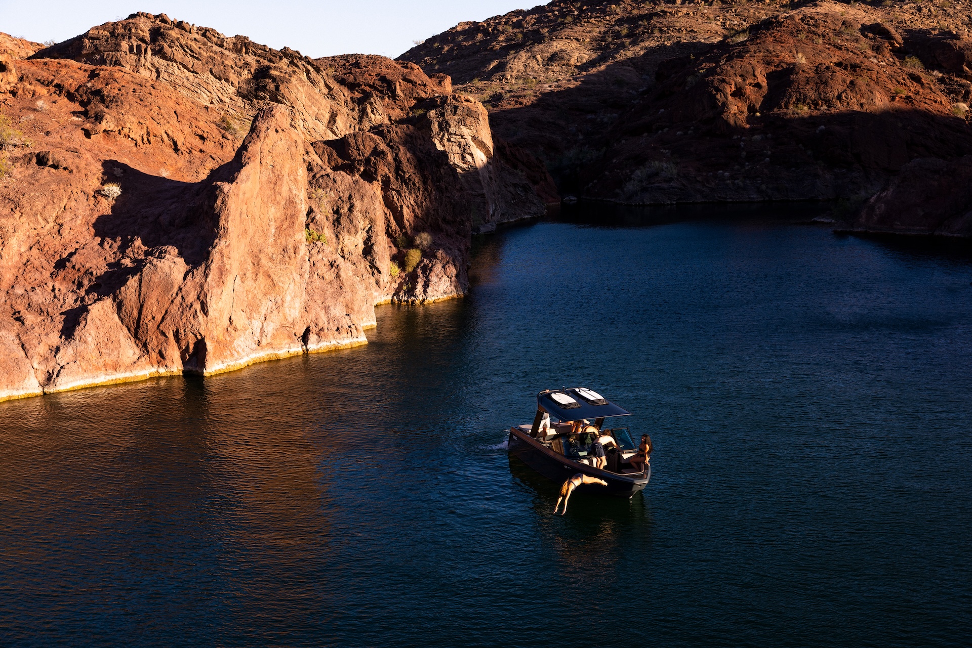 People diving into water from an electric boat. 